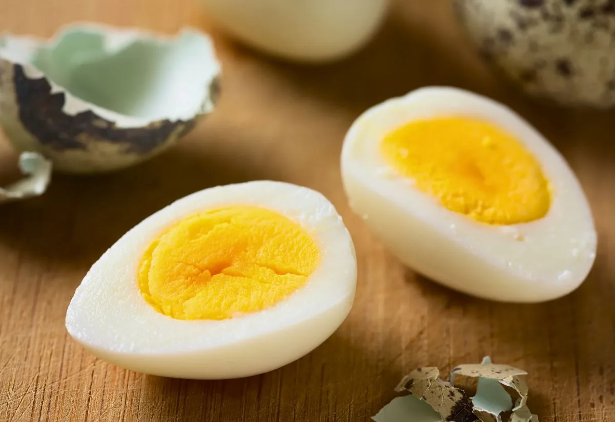 A hard boiled quail egg cut in half with the shell in the background/