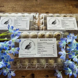Three packs of quail eggs surrounded by forget-me-not flowers.